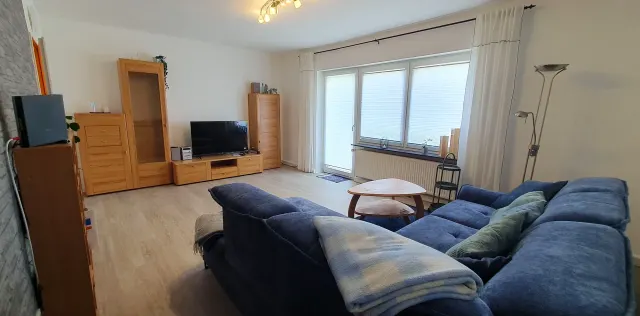 BookNoFees holiday home in Langelsheim – Living room with blue sofa, wooden furniture, and balcony door