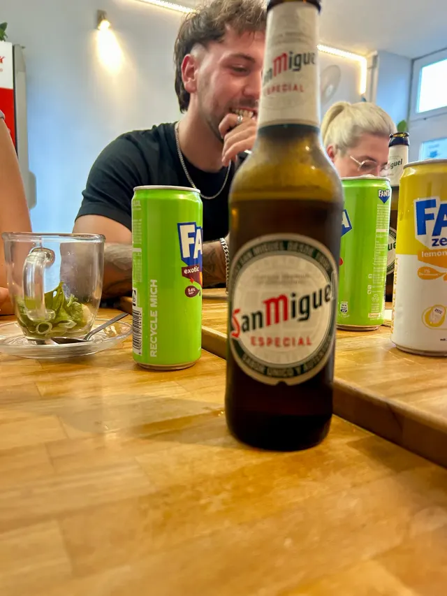 BookNoFees: स्नैक बार – Good morning Vietnam – Aachen – मेज़ पर San Miguel Especial की बोतल और Fanta के कैन, फ़ोटो 2